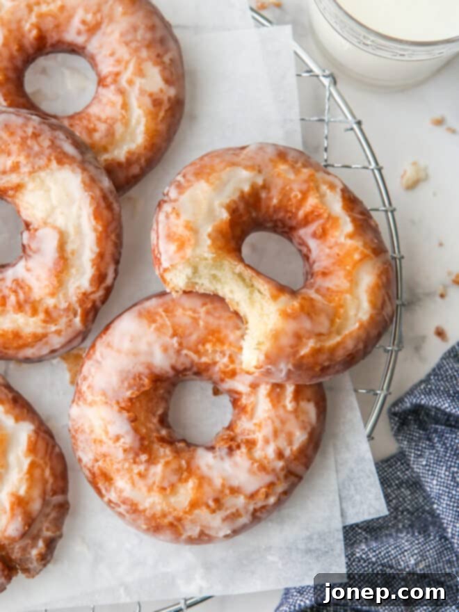 A close-up of a glazed old-fashioned doughnut with a bite taken out of it, revealing the cakey interior.