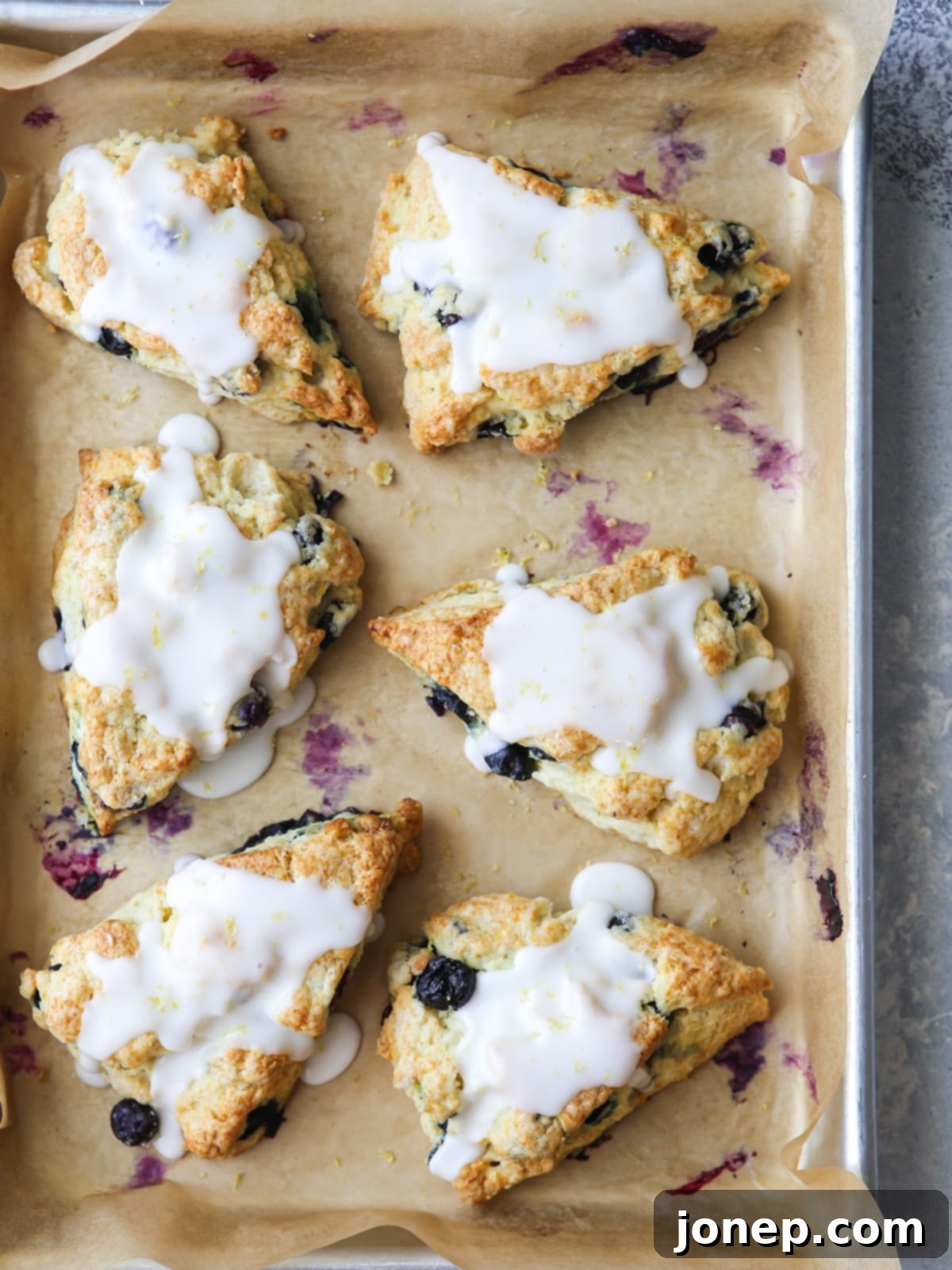 Drizzling tangy lemon glaze over freshly baked lemon blueberry scones