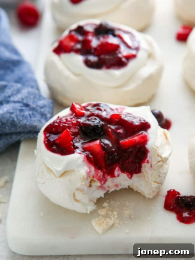 Vibrant Berry Cloud Pavlova 3 bite taken out of a mini pavlova with whipped cream and berry compote