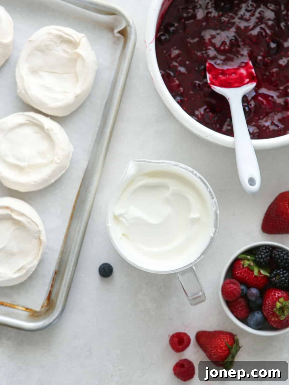 Vibrant Berry Cloud Pavlova 7 mini baked pavlova on a sheet pan, sweetened whipped cream in a cut and berry compote in sauce pan
