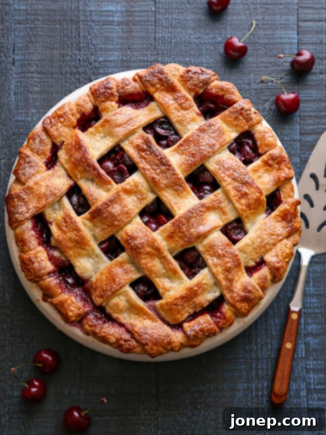 A stunning slice of sweet cherry pie with a golden, flaky crust and a vibrant red, bubbling cherry filling, served with a scoop of vanilla ice cream.