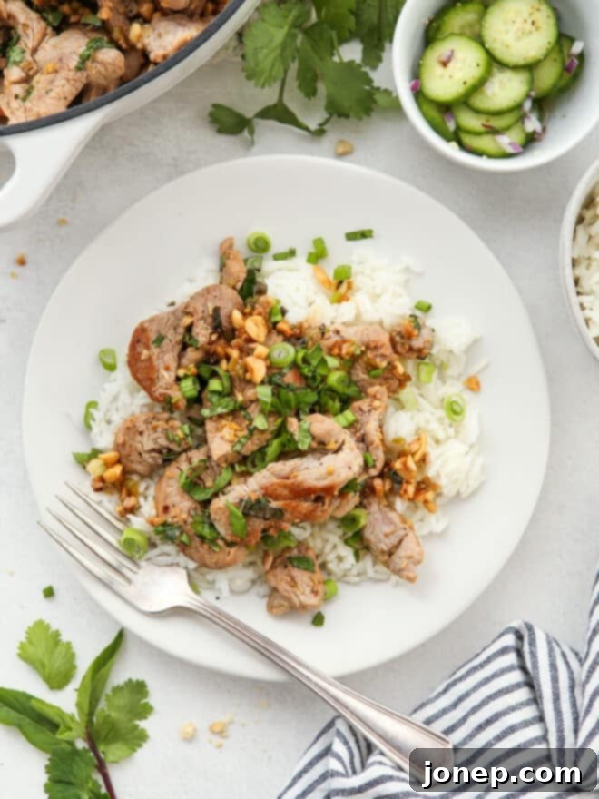 A plate of Thai lemongrass pork served over jasmine rice, garnished with fresh herbs and peanuts.
