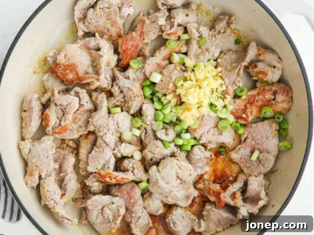 Thai lemongrass pork stir-frying in a skillet, showing the cooking process.