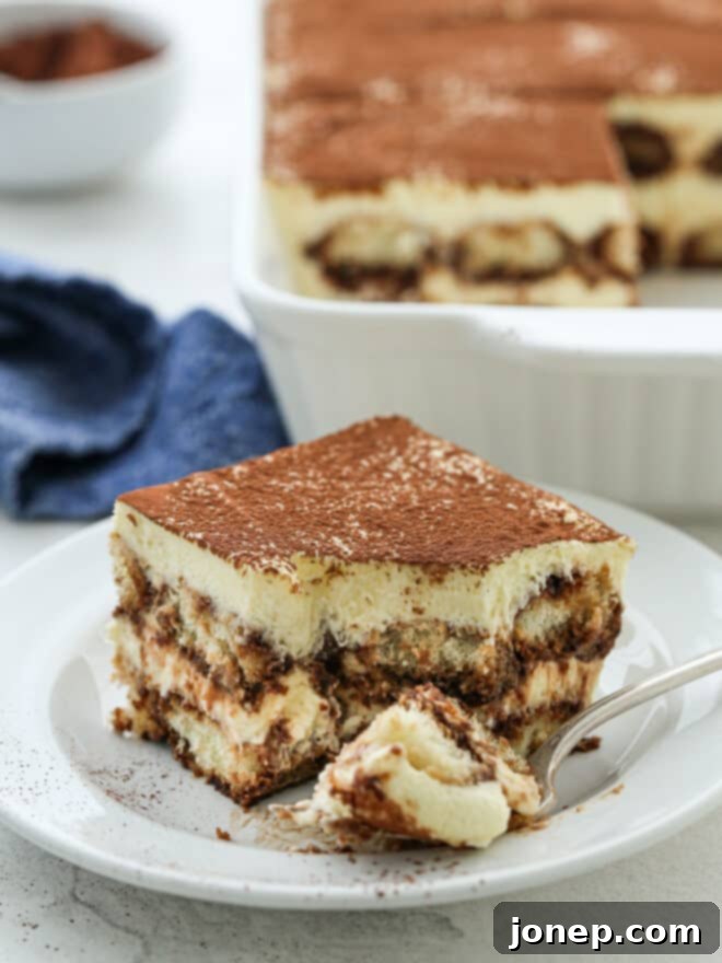 Timeless Italian Tiramisu 4 A close-up shot of a bite taken out of a slice of tiramisu on a plate, highlighting the creamy texture and coffee-soaked ladyfingers.
